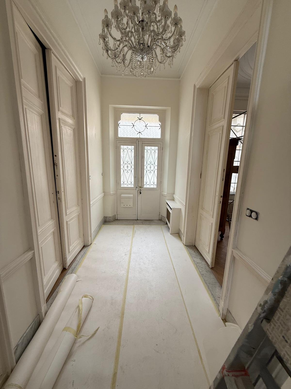 Couloir d'entrée — murs et portes blancs avant travaux, sol protégé